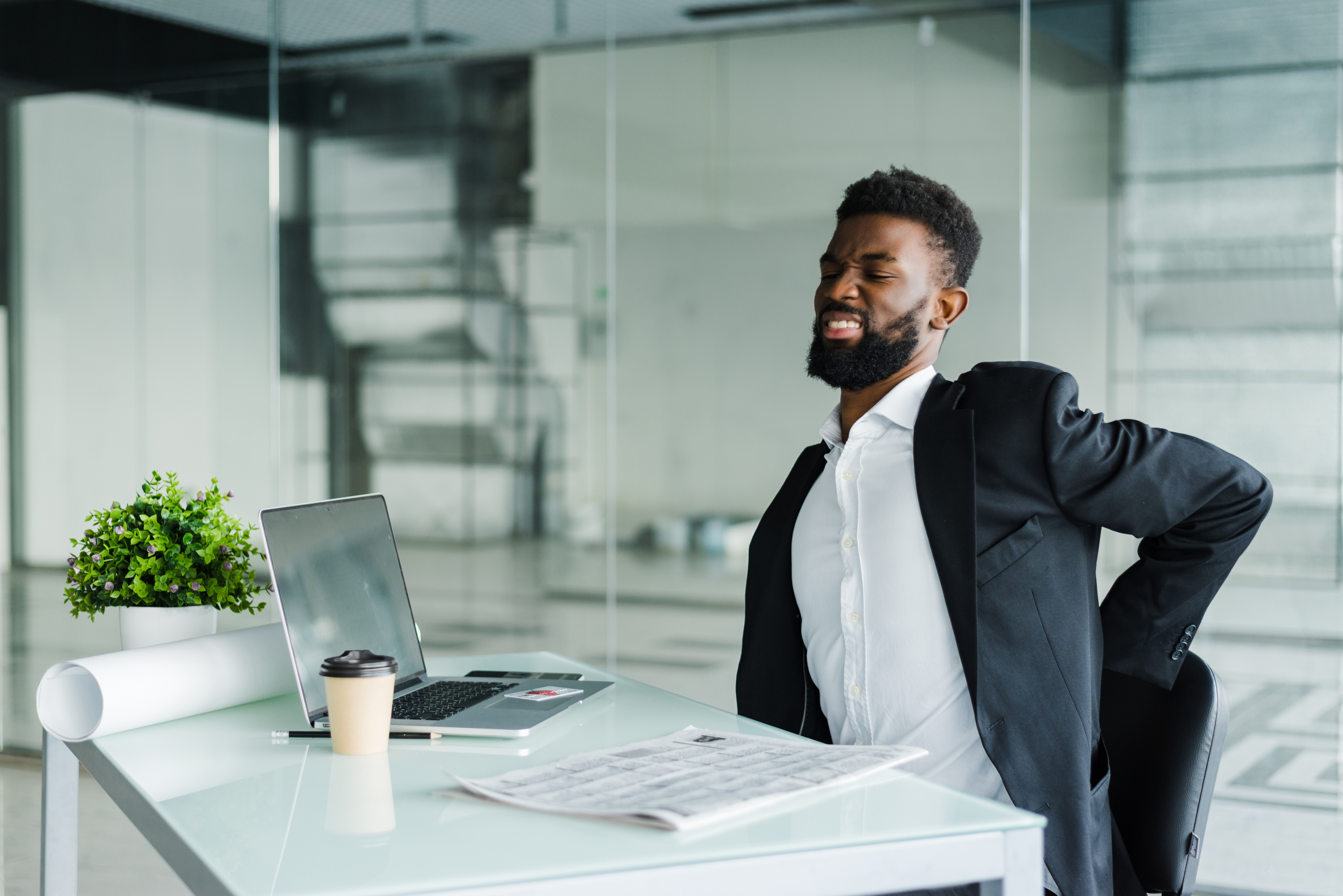 Young Businessman In Office At Desk Suffering From Back Pain